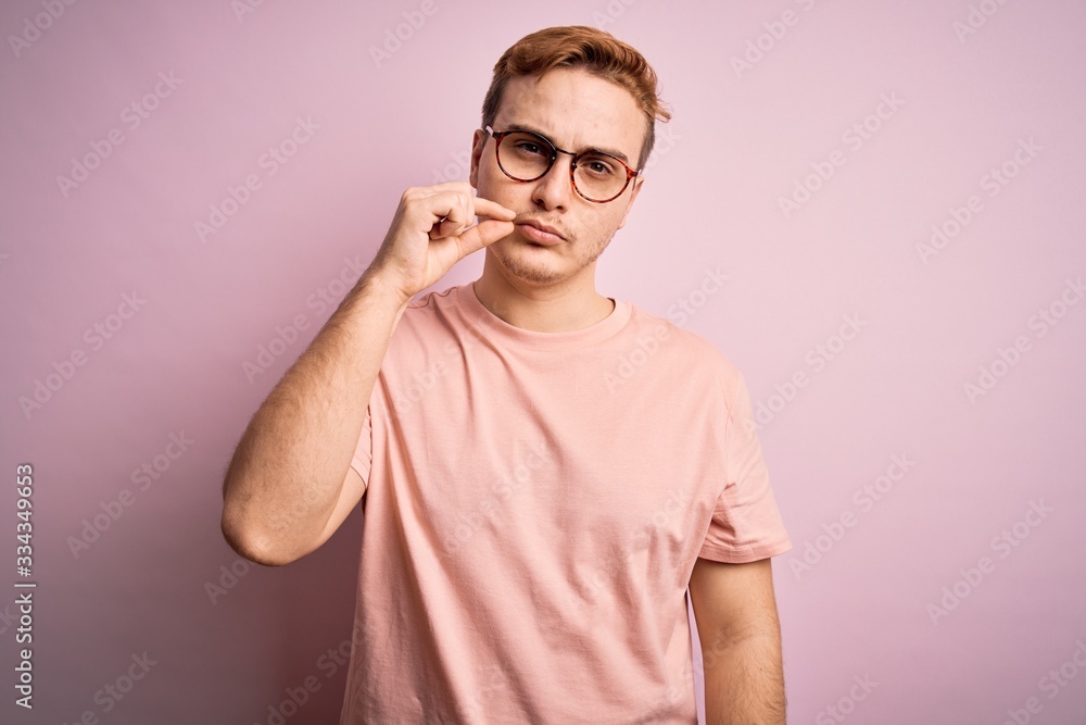 Young handsome redhead man wearing casual t-shirt standing over isolated pink background mouth and lips shut as zip with fingers. Secret and silent, taboo talking Young handsome redhead man wearing casual t-shirt standing over isolated pink background mouth and lips shut as zip with fingers. Secret and silent, taboo talking