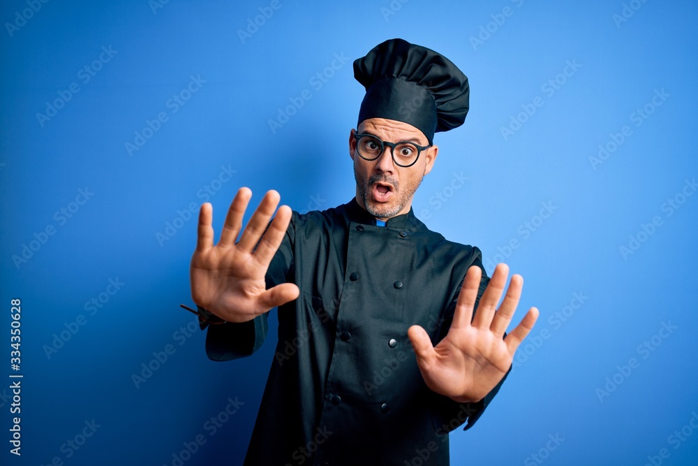 Young handsome chef man wearing cooker uniform and hat over isolated blue background doing stop gesture with hands palms, angry and frustration expression Young handsome chef man wearing cooker uniform and hat over isolated blue background doing stop gesture with hands palms, angry and frustration expression