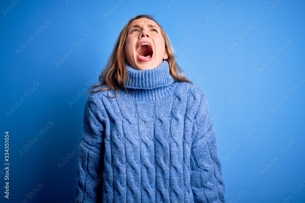 Young beautiful blonde woman wearing casual turtleneck sweater over blue background angry and mad screaming frustrated and furious, shouting with anger. Rage and aggressive concept. Young beautiful blonde woman wearing casual turtleneck sweater over blue background angry and mad screaming frustrated and furious, shouting with anger. Rage and aggressive concept.