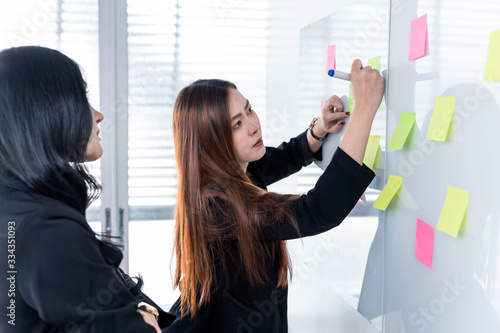 Business woman using post it note on glossy white board.