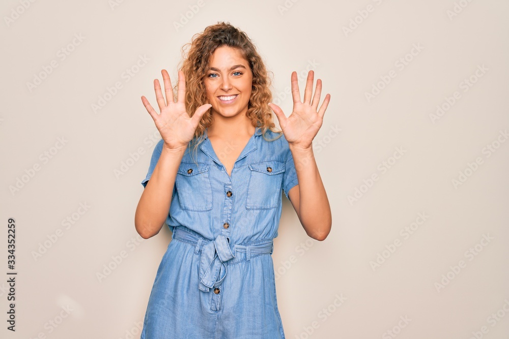 Young beautiful woman with blue eyes wearing casual denim dress over white background showing and pointing up with fingers number ten while smiling confident and happy. Young beautiful woman with blue eyes wearing casual denim dress over white background showing and pointing up with fingers number ten while smiling confident and happy.
