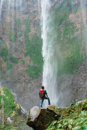 Happy man standing on the cliff to watch Tumpak Sewu waterfall scenic nature beauty.