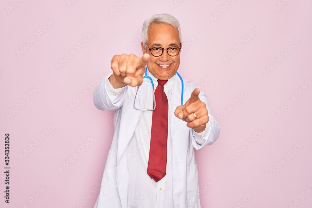 Middle age senior grey-haired doctor man wearing stethoscope and professional medical coat pointing to you and the camera with fingers, smiling positive and cheerful Middle age senior grey-haired doctor man wearing stethoscope and professional medical coat pointing to you and the camera with fingers, smiling positive and cheerful