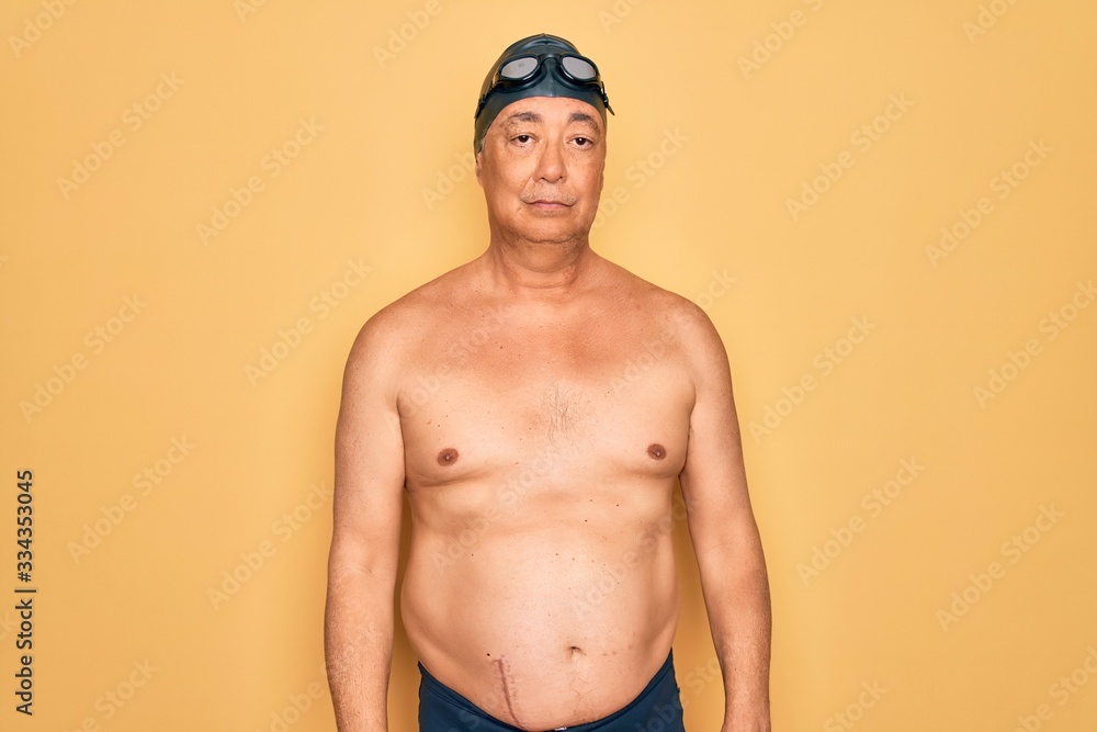 Middle age senior grey-haired swimmer man wearing swimsuit, cap and goggles looking sleepy and tired, exhausted for fatigue and hangover, lazy eyes in the morning.
