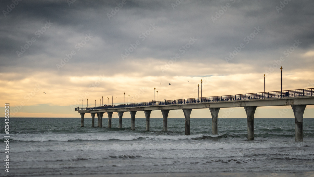 Massive concrete pier leading to horizon surrounded by ocean. Shot made during sunset in New Brighton Beach in Christchurch, New Zealand