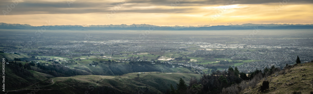 Panoramic sunset shot of city with mountains backdrop. Shot at Port Hills above Christchurch, New Zealand