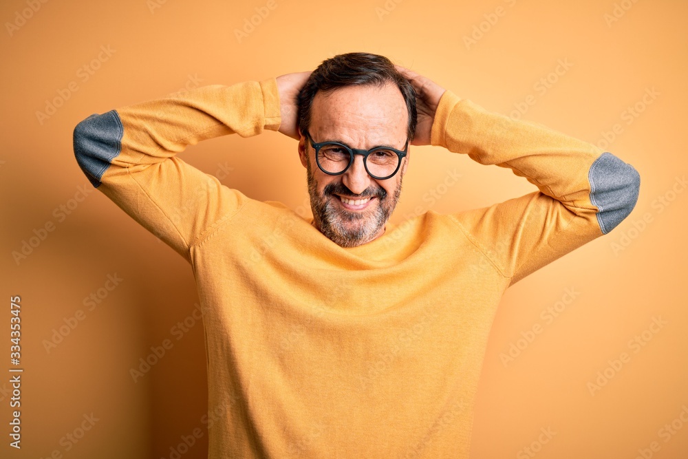 Middle age hoary man wearing casual sweater and glasses over isolated yellow background relaxing and stretching, arms and hands behind head and neck smiling happy Middle age hoary man wearing casual sweater and glasses over isolated yellow background relaxing and stretching, arms and hands behind head and neck smiling happy
