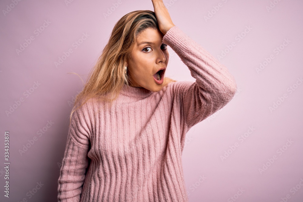 Young beautiful blonde woman wearing casual pink sweater over isolated background surprised with hand on head for mistake, remember error. Forgot, bad memory concept. Young beautiful blonde woman wearing casual pink sweater over isolated background surprised with hand on head for mistake, remember error. Forgot, bad memory concept.
