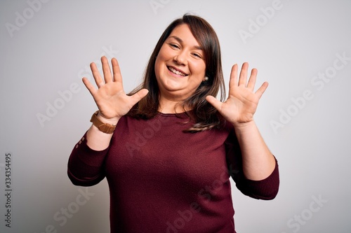 Beautiful brunette plus size woman wearing casual sweater over isolated white background showing and pointing up with fingers number ten while smiling confident and happy.