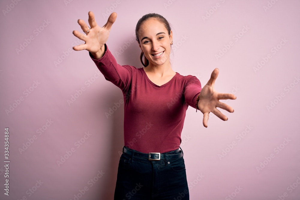Young beautiful woman wearing casual t-shirt standing over isolated pink background looking at the camera smiling with open arms for hug. Cheerful expression embracing happiness. Young beautiful woman wearing casual t-shirt standing over isolated pink background looking at the camera smiling with open arms for hug. Cheerful expression embracing happiness.