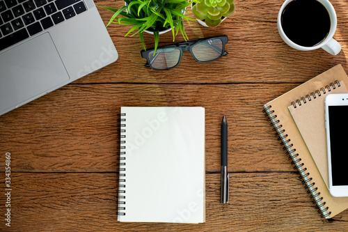 Top view from above of Blank notebook with laptop  glasses and coffee on wood table background. Workplace for creative work of designer at home. Flat lay  Business-finance concept with copy space.