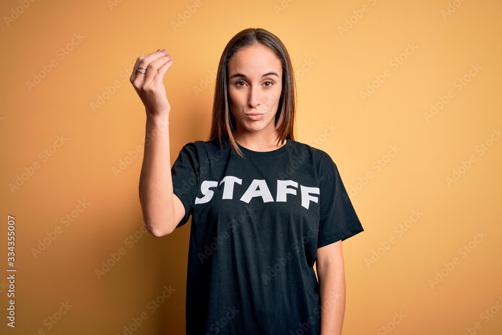 Young beautiful worker woman wearing staff uniform t-shirt over isolated yellow background Doing Italian gesture with hand and fingers confident expression Young beautiful worker woman wearing staff uniform t-shirt over isolated yellow background Doing Italian gesture with hand and fingers confident expression