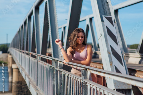 Pretty young woman posing on the old rusty transport bridge over the river during sunset.