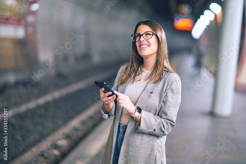 Young beautiful woman smiling happy and confident. Standing with smile on face using smartphone at platform of train station