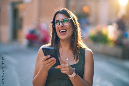 Young beautiful woman smiling happy and confident. Standing with smile on face using smartphone at the city