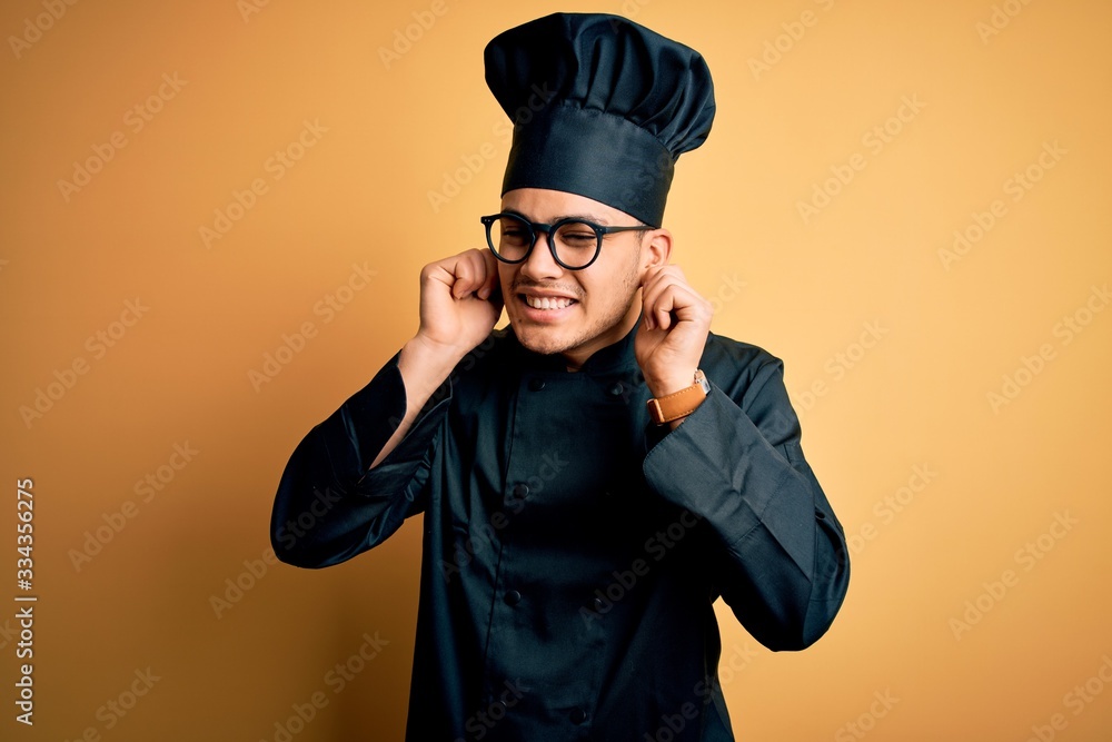 Young brazilian chef man wearing cooker uniform and hat over isolated yellow background Smiling pulling ears with fingers, funny gesture. Audition problem Young brazilian chef man wearing cooker uniform and hat over isolated yellow background Smiling pulling ears with fingers, funny gesture. Audition problem
