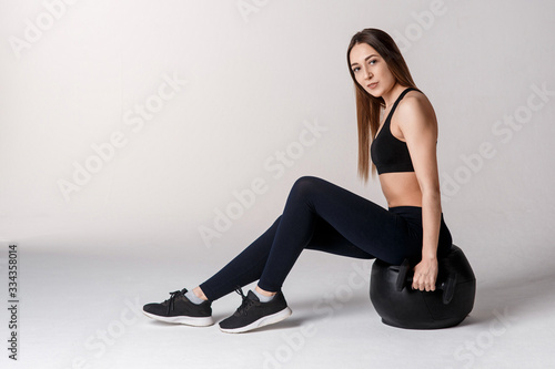 Athletic woman doing exercise with med ball. Photo of sporty latin woman in fashionable sportswear on black background. Strength and motivation