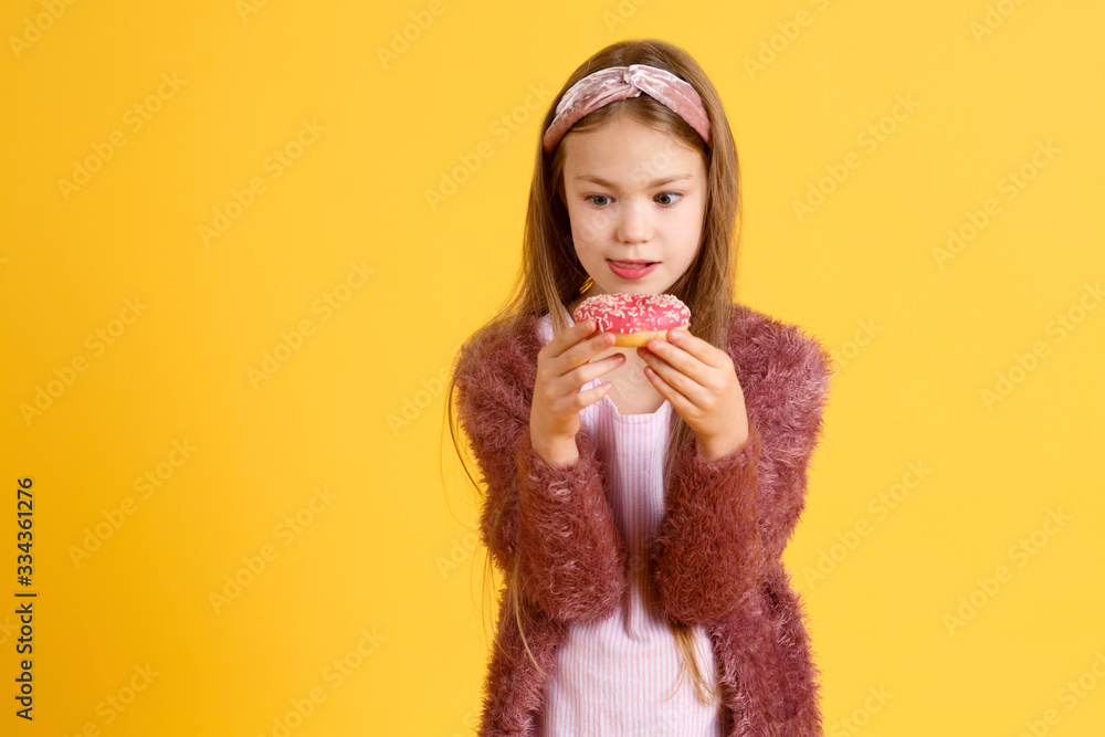 Crazy cheerful blonde girl in birthday hat smiling, having fun and looking through two red donuts on her eyes. Sweets. Yellow studio background Crazy cheerful blonde girl in birthday hat smiling, having fun and looking through two red donuts on her eyes. Sweets. Yellow studio background