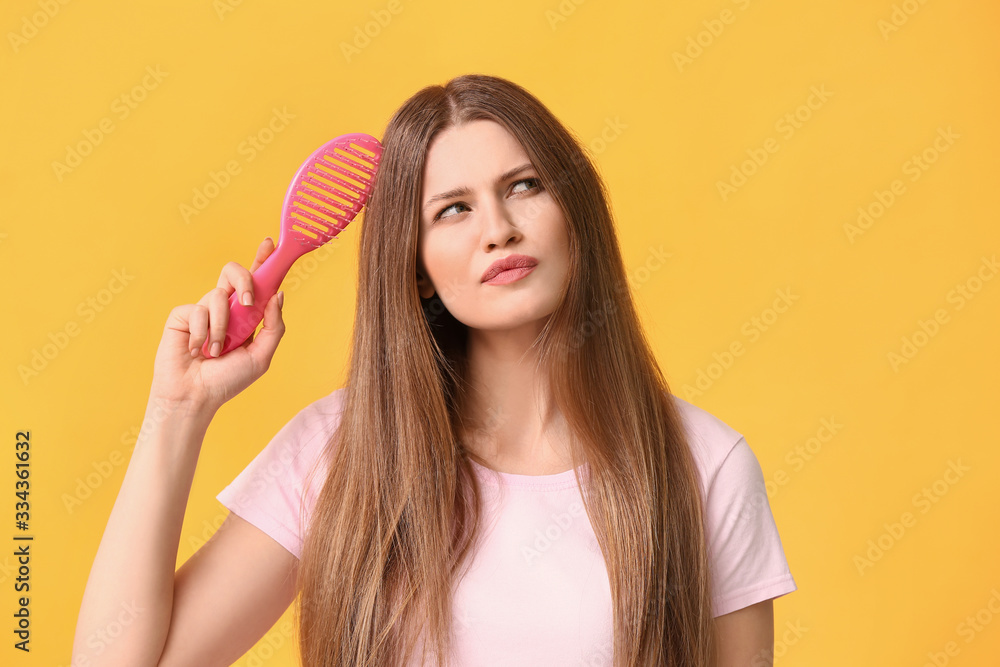 Thoughtful young woman brushing hair on color background Thoughtful young woman brushing hair on color background