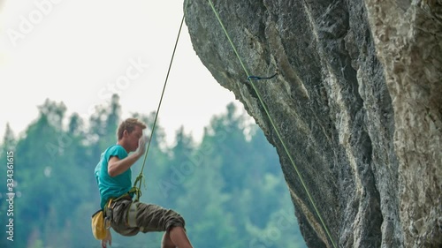 man climbing a vertical cliff reach for an handhold but fails and falls