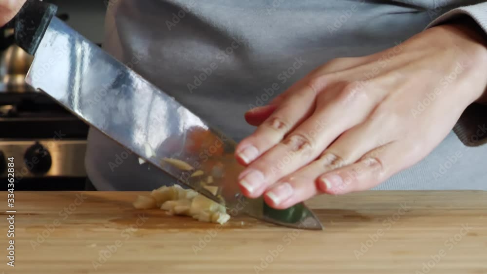 Lady using rocking knife to finely slice and chop garlic cloves on chopping board Lady using rocking knife to finely slice and chop garlic cloves on chopping board