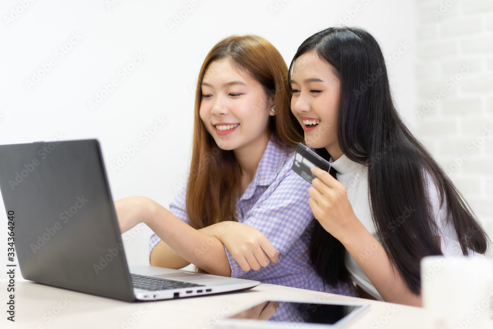 Happy best friends laughing during watching funny videos on internet social media life . Young Asian female doing online shopping through laptop and credit card at home. Happy best friends laughing during watching funny videos on internet social media life . Young Asian female doing online shopping through laptop and credit card at home.