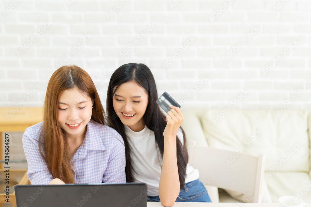 Happy best friends laughing during watching funny videos on internet social media life . Young Asian female doing online shopping through laptop and credit card at home. Happy best friends laughing during watching funny videos on internet social media life . Young Asian female doing online shopping through laptop and credit card at home.