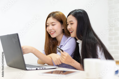 Happy best friends laughing during watching funny videos on internet social media life . Young Asian female doing online shopping through laptop and credit card at home.