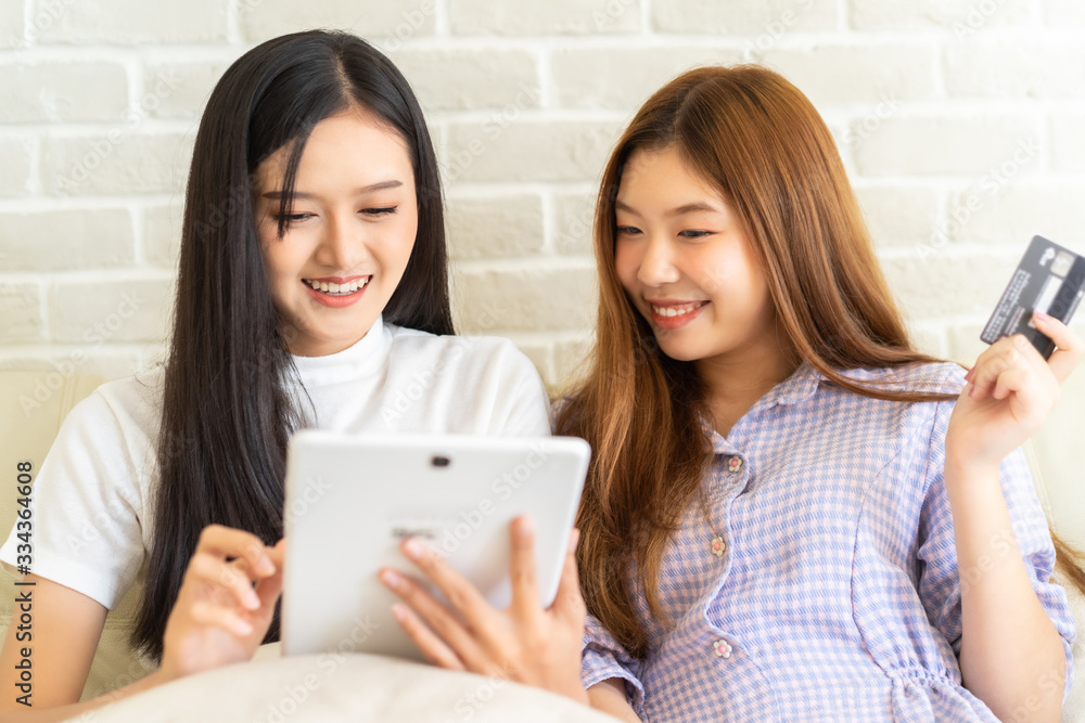 Happy best friends laughing during watching funny videos on internet social media life . Young Asian female doing online shopping through laptop and credit card at home. Happy best friends laughing during watching funny videos on internet social media life . Young Asian female doing online shopping through laptop and credit card at home.
