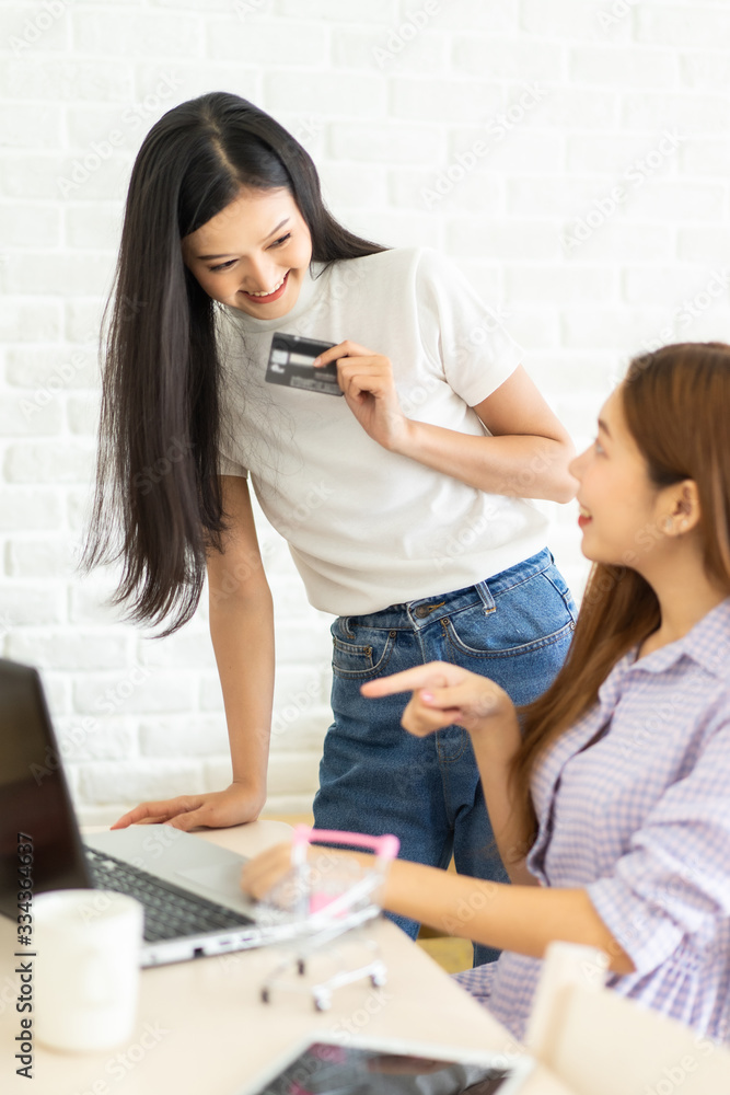 Happy best friends laughing during watching funny videos on internet social media life . Young Asian female doing online shopping through laptop and credit card at home. Happy best friends laughing during watching funny videos on internet social media life . Young Asian female doing online shopping through laptop and credit card at home.
