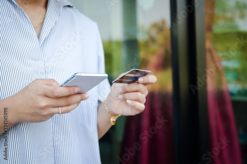 Girl holding a credit card to fill out on the smartphone To buy products online via the internet. Concept of spending money with modern technology