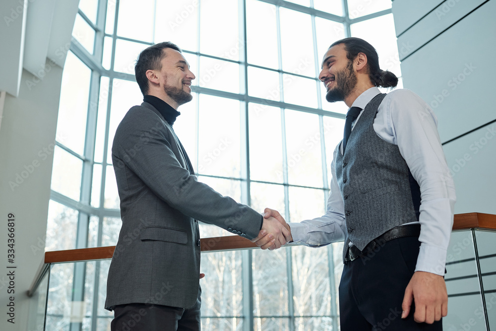 Two young successful busines partners greeting each other by handshake Two young successful busines partners greeting each other by handshake