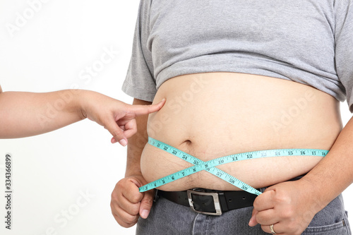 Fat man, very big belly, standing, using tape measure around his waist. Concept of weight loss, prevention of disease. White background