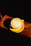 A bright vertical photo of a beautiful yellow cup of cappuccino on a wooden table in direct sun light, deep shadows.
