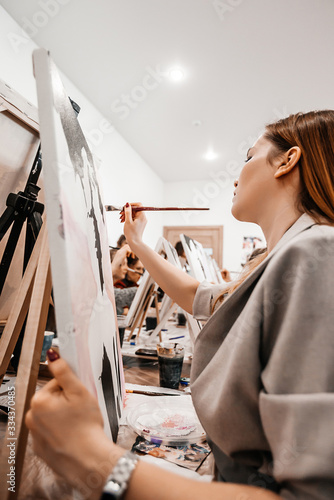 A young woman painstakingly draws her picture with brushes on easels in an art class. learning to draw , art school, creativity and the concept of people