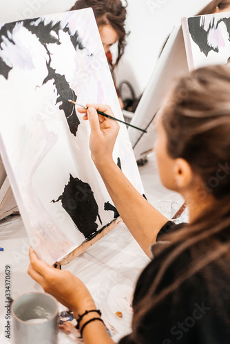 A young woman painstakingly draws her picture with brushes on easels in an art class. learning to draw , art school, creativity and the concept of people