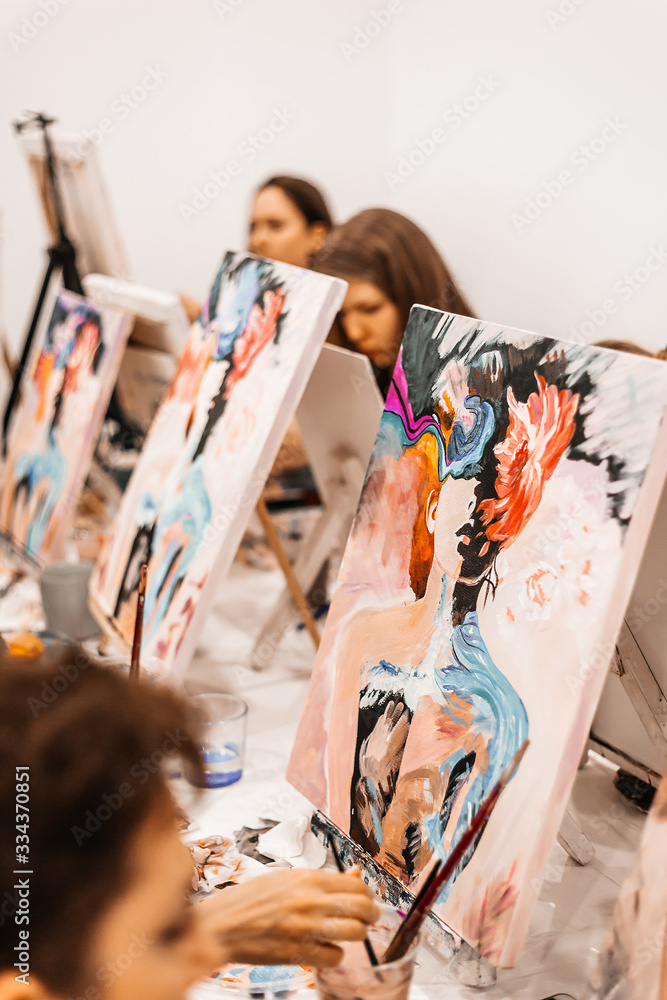 Obraz premium Young women paint with brushes on easels in art class. art school, creativity and people concept
