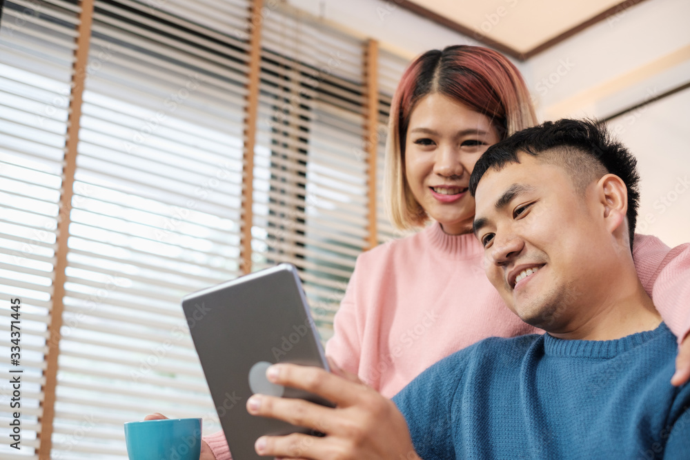 Asian couple watching video live on tablet on sofa in living room at home.lover spending time together Asian couple watching video live on tablet on sofa in living room at home.lover spending time together