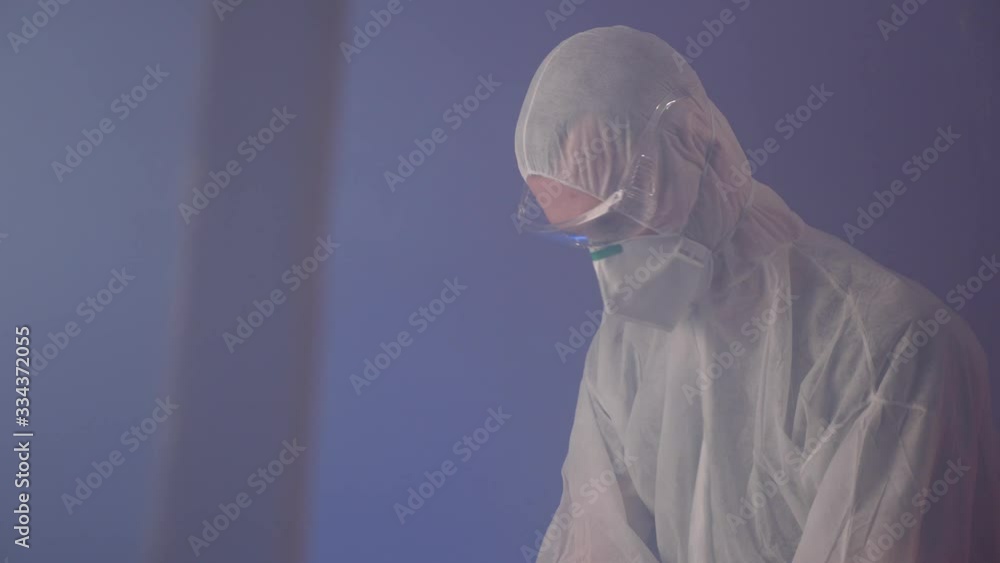 Specialist in protective suit, face mask and goggles works on laptop with passion and commitment; medium shot Specialist in protective suit, face mask and goggles works on laptop with passion and commitment; medium shot