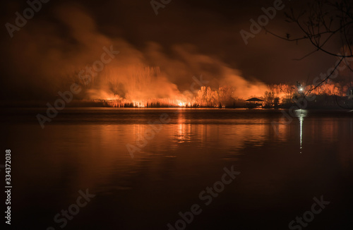 Night forest fire, reflected on the water surface of the river