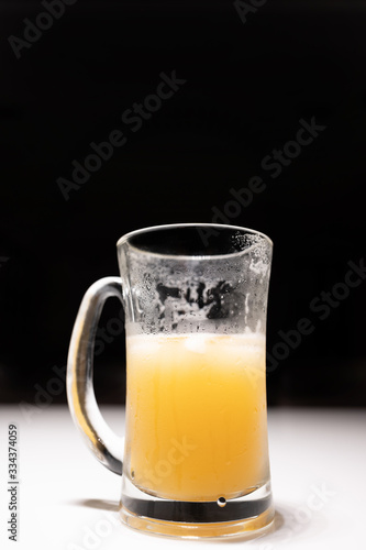 Tall glass with a handle and half a amber beer There is a drop of water on the side of the glass from the coldness. On a white table with black background Dark tone image