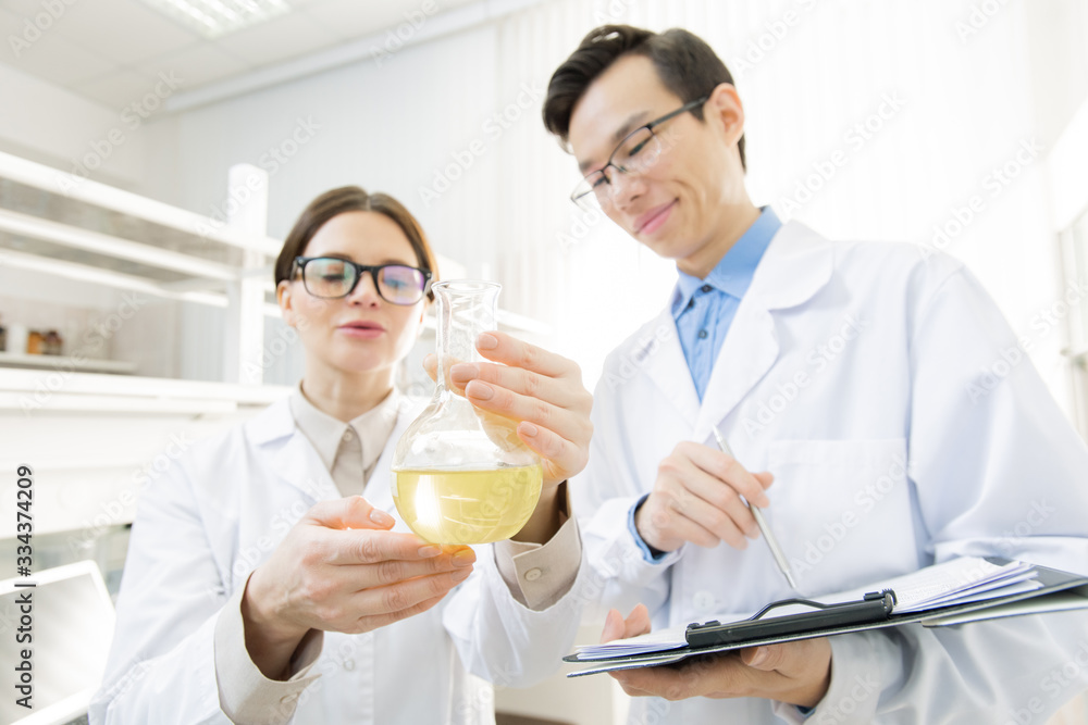 Female researcher holding beak with yellow fluid while showing it to colleague
