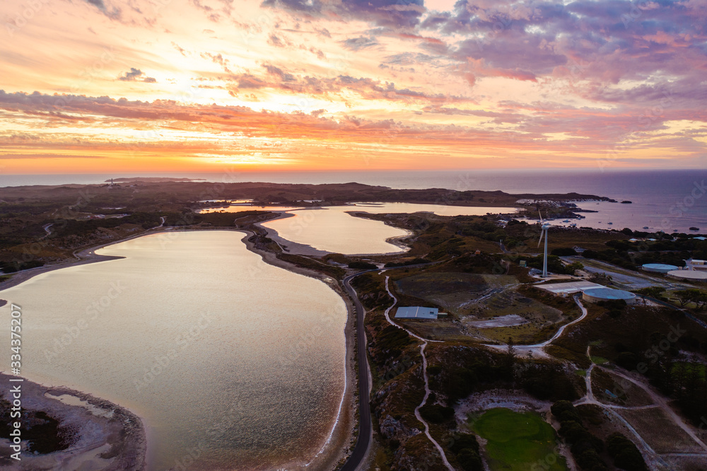 Aerial drone image of Rottnest Island lakes at sunset. The golden light covers the island and the lakes light up, reflecting the clouds. 