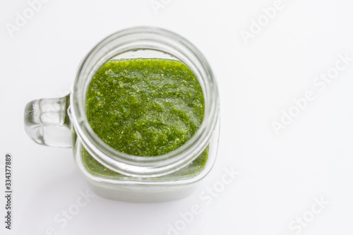 glass jar glass with green fresh smoothie and raw vegetables on white background
