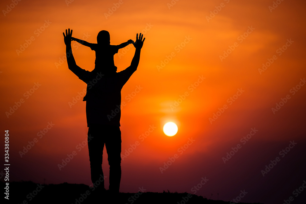 Fototapeta premium silhouette of a family with a boy riding his father's neck happily against the sunset sky