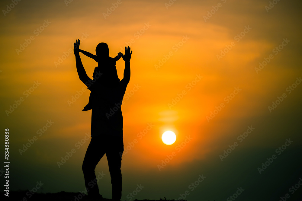 Fototapeta premium silhouette of a family with a boy riding his father's neck happily against the sunset sky