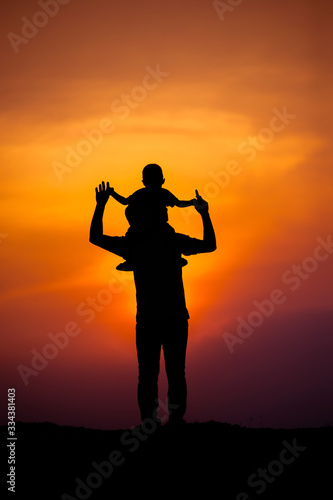 silhouette of a family with a boy riding his father's neck happily against the sunset sky © stcom