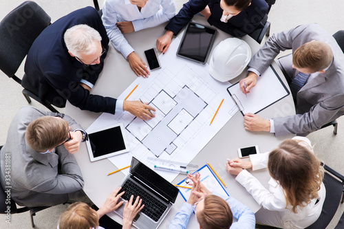 construction business, architecture and building concept - group of architects with laptop computer discussing blueprint at office