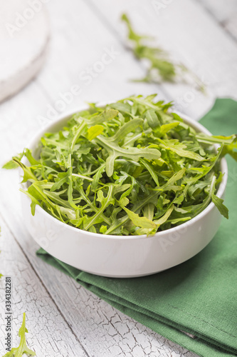 Fresh green arugula leaves on white bowl, rucola rocket salad on wooden rustic background with place for text. Selective focus,  healthy food, diet. Nutrition concept