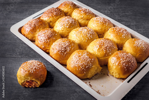 Baking tray with freshly baked buns sprinkled with chopped coconut on a gray background.
